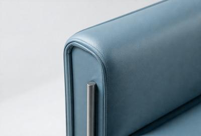 The primary subject of the image is a blue leather chair with a silver metal armrest. The chair is positioned on a white surface, which serves as the background. The visual style of the image is a photo, capturing the details of the chair and its armrest. The dominant colors in the image are blue and silver, creating a modern and sleek appearance.
