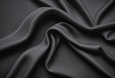 The primary subject of the image is a close-up of a black fabric, possibly a piece of cloth or a curtain. The setting is a dark background, which emphasizes the fabric's texture and color. The visual style appears to be a close-up or a detailed view of the fabric. The colors and mood of the image are predominantly dark, with the black fabric being the main focus.