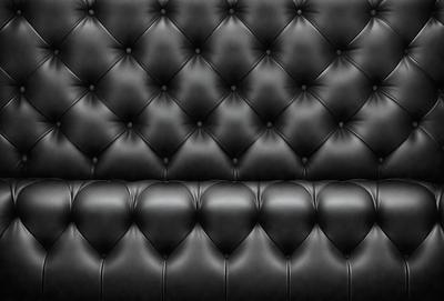 The primary subject of the image is a black leather couch. The setting is a black background, which emphasizes the couch's design. The visual style is a close-up of the couch, showcasing its details. The colors and mood of the image are dark and sophisticated, with the black leather creating a luxurious and elegant atmosphere.