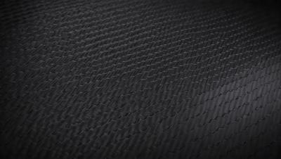 The primary subject of the image is a close-up of a black, textured surface. The setting appears to be a dark room, with the surface being the main focus of the image. The visual style is a close-up, which emphasizes the texture and pattern of the surface. The colors in the image are predominantly black, creating a moody atmosphere.