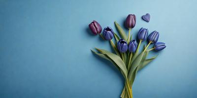 The primary subject of the image is a bouquet of purple tulips. The setting is a blue wall, which serves as the backdrop for the flowers. The visual style is a close-up of the flowers, showcasing their vibrant colors and details. The overall atmosphere is serene and elegant, as the purple tulips are the main focus of the image.