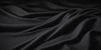 The primary subject of the image is a black fabric, which appears to be a piece of cloth or a curtain. The setting is a dark background, which contrasts with the black fabric. The visual style is a close-up of the fabric, showcasing its texture and details. The colors and mood of the image are predominantly dark, with the black fabric being the main focus.