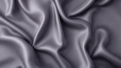 The primary subject of the image is a close-up of a piece of fabric, which appears to be a gray or black silk material. The setting is a dark background, which emphasizes the fabric's texture and color. The visual style is a close-up, focusing on the details of the fabric. The colors and mood of the image are dark and moody, with the fabric's texture and color being the main focus.