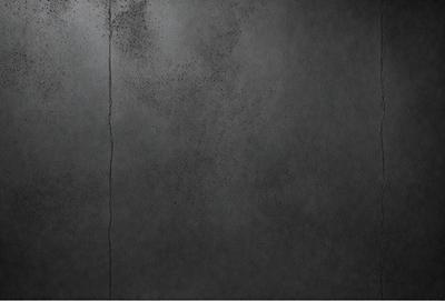 The primary subject of the image is a wall with a crack in it. The setting is a dark room, and the visual style appears to be a photo. The colors and mood of the image are dark and moody, with the crack in the wall being the main focal point.