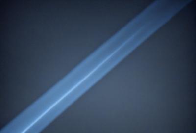 The primary subject of the image is a blue light, which appears to be a long, thin line. The setting is a dark background, which contrasts with the blue light. The visual style of the image is a close-up of the blue light, emphasizing its shape and texture. The colors and mood of the image are predominantly dark and moody, with the blue light serving as a focal point against the black background.