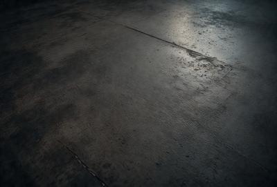 The primary subject of the image is a large, grey, concrete floor. The setting is a room with a concrete surface, and the visual style is a photo. The colors and mood of the image are predominantly dark and moody, with the grey concrete floor being the main focus.