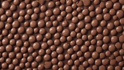 The primary subject of the image is a close-up of a chocolate surface with a pattern of chocolate balls or marshmallows. The setting is a chocolate-covered surface, and the visual style appears to be a close-up photo of the chocolate. The colors and mood of the image are predominantly brown, giving it a rich and indulgent atmosphere.