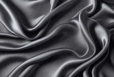 The primary subject of the image is a close-up of a piece of fabric, which appears to be a gray or black silk material. The setting is a dark background, which emphasizes the fabric's texture and color. The visual style is a close-up, focusing on the details of the fabric. The colors and mood of the image are dark and moody, with the fabric's texture and color being the main focus.
