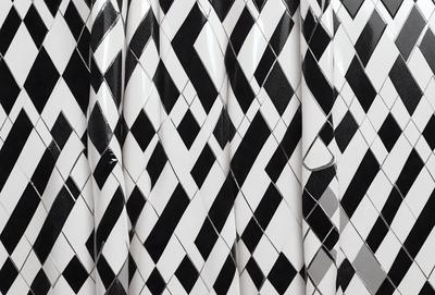 The primary subject of the image is a patterned curtain with a black and white checkered design. The setting is a room with a white wall behind the curtain. The visual style is a close-up of the curtain, showcasing its intricate pattern. The colors and mood of the image are predominantly black and white, giving it a classic and elegant appearance.