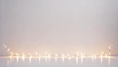 The primary subject of the image is a string of lights, which are illuminated and create a visually appealing display. The lights are arranged in a row, creating a sense of depth and dimension. The setting is a white wall, which serves as a clean and uncluttered backdrop for the lights. The visual style of the image is a combination of digital art and illustration, as the lights are depicted in a realistic manner while still maintaining a sense of artistic expression. The colors and mood of the