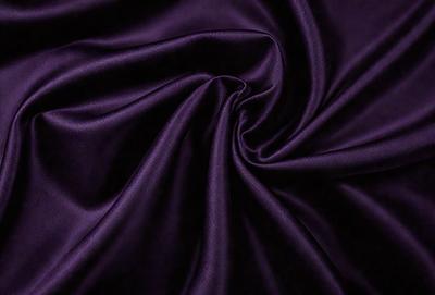 The primary subject of the image is a purple fabric, which is the main object, scene, or focus of the image. The setting or background is a dark background, which contrasts with the purple fabric. The visual style of the image is a close-up of the purple fabric, showcasing its texture and pattern. The colors and mood of the image are predominantly purple, creating a sense of elegance and sophistication.