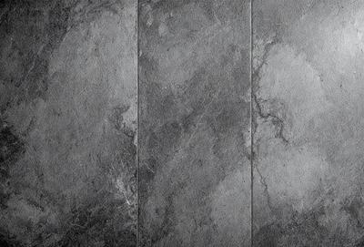 The primary subject of the image is a close-up of a grey tile wall. The setting is a room with a grey tile floor. The visual style is a photo, and the dominant colors are grey and black. The overall atmosphere is a combination of modern and industrial, with a touch of elegance.