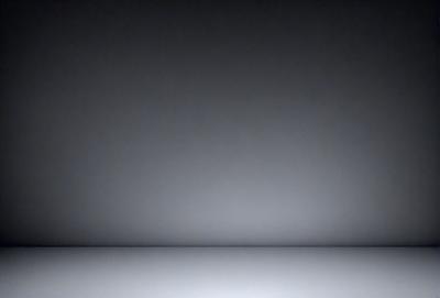 The primary subject of the image is a large, empty room with a white wall. The setting is a dark room, possibly a basement, with a black background. The visual style is a black and white photo, giving the image a classic and timeless appearance. The colors and mood are predominantly dark and moody, creating a sense of mystery and solitude.