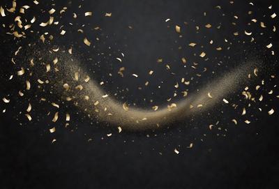 The primary subject of the image is a close-up of gold confetti or glitter, which is the main object, scene, or focus of the image. The setting is a dark background, which contrasts with the gold confetti. The visual style is a close-up of the confetti, giving a detailed view of the glitter. The colors and mood of the image are predominantly gold and glittery, creating a festive and celebratory atmosphere.