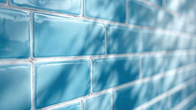 The primary subject of the image is a blue brick wall. The setting is an outdoor environment, with a tree visible in the background. The visual style is a photo, capturing the brick wall and its surroundings. The dominant colors are blue and green, creating a calm and serene atmosphere.
