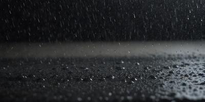 The primary subject of the image is a rainy street scene. The setting is a dark, wet road with rain falling down. The visual style is a photo, capturing the rainy atmosphere. The colors and mood are dominated by the dark, wet road and the falling rain, creating a moody and atmospheric scene.