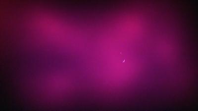 The primary subject of the image is a pink background with a crescent moon in the center. The setting appears to be a dark, possibly purple, environment. The visual style of the image is a combination of a photo and a digital art or illustration. The dominant colors in the image are pink and purple, creating a warm and moody atmosphere.