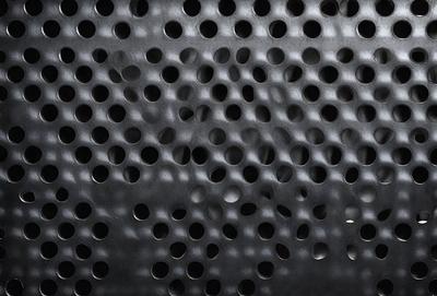 The primary subject of the image is a close-up of a metal surface with a pattern of holes. The setting is a black background, and the visual style appears to be a photo. The dominant colors are black and silver, creating a sleek and modern atmosphere.