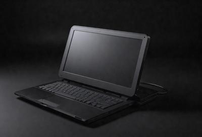 The primary subject of the image is a laptop computer. The laptop is open and sitting on a black surface, which appears to be a table. The setting is a dark room, creating a moody atmosphere. The visual style of the image is a photo, capturing the details of the laptop and its surroundings.