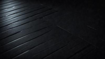 The primary subject of the image is a wooden floor with a black surface. The setting is a dark room, and the visual style appears to be a photo. The colors and mood of the image are predominantly dark, with a sense of mystery or intrigue.