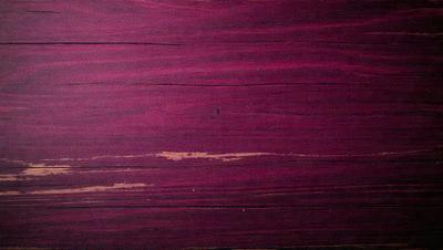 The primary subject of the image is a wooden surface with a purple hue. The setting is a wooden wall, and the visual style appears to be a photo. The dominant colors are purple and brown, creating a moody atmosphere.