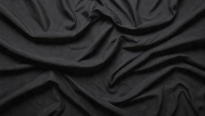The primary subject of the image is a black fabric, which appears to be a piece of cloth or a curtain. The setting is a dark room, and the visual style is a close-up of the fabric. The colors and mood of the image are predominantly dark, with the black fabric being the main focus.