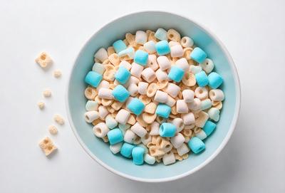 The primary subject of the image is a bowl filled with marshmallows. The marshmallows are white and blue, and they are arranged in a visually appealing manner. The bowl is placed on a white surface, which provides a clean and simple backdrop for the marshmallows. The overall atmosphere of the image is cheerful and fun, as the marshmallows evoke a sense of outdoor recreation and relaxation.