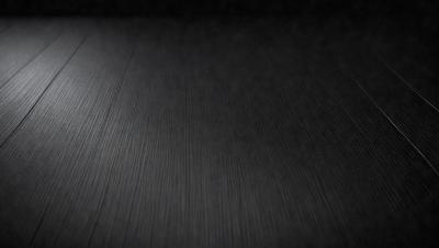 The primary subject of the image is a black surface, which appears to be a table or a countertop. The setting is a dark room, and the visual style is a close-up of the black surface. The colors and mood of the image are predominantly dark and moody, with the black surface being the main focus.