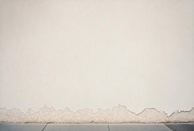 The primary subject of the image is a white wall with a pattern of white and brown lines. The setting is a room with a tiled floor. The visual style is a photo, and the colors and mood are predominantly white and neutral, giving the image a clean and minimalist appearance.