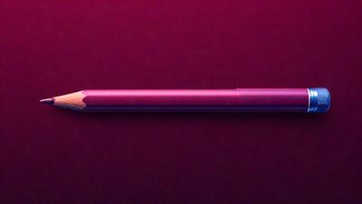 The primary subject of the image is a pink pencil. The setting is a red background, which creates a contrasting color scheme. The visual style is a close-up of the pencil, showcasing its details. The colors and mood of the image are predominantly pink and red, giving it a warm and vibrant atmosphere.