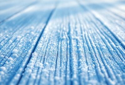 The primary subject of the image is a snow-covered wooden surface. The setting is a snowy environment, with the background featuring a blue sky. The visual style is a photo, capturing the beauty of the snow-covered wooden surface. The colors and mood of the image are predominantly blue and cold, reflecting the winter season and the snowy landscape.