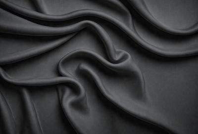 The primary subject of the image is a close-up of a black fabric, possibly a piece of clothing or a curtain. The setting is a dark background, which emphasizes the fabric's texture and pattern. The visual style is a close-up, which highlights the fabric's details. The colors and mood of the image are predominantly dark, with the black fabric being the main focus.