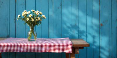 The primary subject of the image is a vase filled with flowers, placed on a table. The setting is a blue wall, which serves as the backdrop for the scene. The visual style is a photo, capturing the beauty of the flowers and the table. The colors in the image are predominantly blue and white, creating a calm and serene atmosphere.
