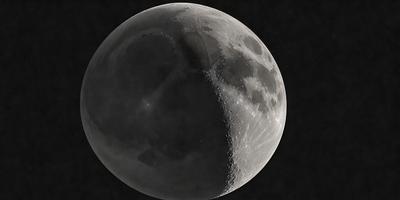 The primary subject of the image is a close-up of a moon, with a black background. The visual style appears to be a photo, as the moon is captured in detail. The colors and mood of the image are predominantly dark, with the moon being the main focus.