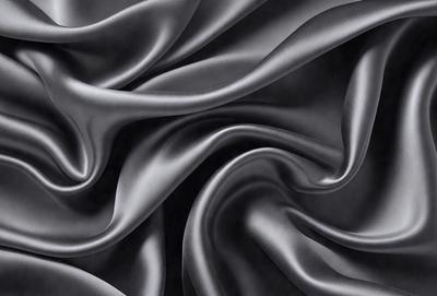 The primary subject of the image is a close-up of a black fabric, possibly a piece of clothing or a curtain. The setting is a dark background, which emphasizes the fabric's texture and pattern. The visual style appears to be a photo, as the fabric is captured in detail. The colors and mood of the image are predominantly dark, with the black fabric being the main focus.
