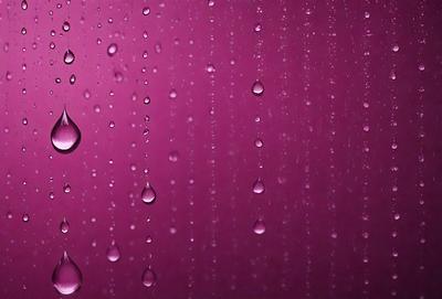 The primary subject of the image is a purple wall with water droplets falling on it. The setting is a room with a purple wall, and the visual style is a photo. The colors and mood of the image are predominantly purple, creating a calm and serene atmosphere.