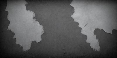 The primary subject of the image is a wall with a peeling paint surface. The setting is a room with a grey background. The visual style is a black and white photo. The dominant colors are grey and black, creating a moody atmosphere.