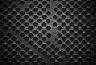 The primary subject of the image is a pattern of small circles, which are arranged in a dense and intricate manner. The setting is a black background, which contrasts with the circles, making them stand out. The visual style is a close-up of the pattern, showcasing the details of the circles. The colors and mood of the image are predominantly dark, with the small circles being the main focus and source of visual interest.