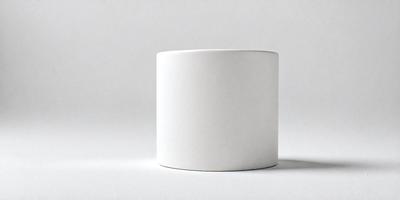 The primary subject of the image is a white ceramic cup. The cup is placed on a white surface, which could be a table or a counter. The visual style of the image is a photo, capturing the cup in its natural setting. The colors and mood of the image are predominantly white, giving it a clean and minimalist appearance.