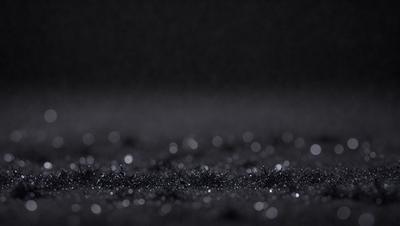 The primary subject of the image is a black background with a pattern of glittering specks. The setting is a dark room, and the visual style is a close-up of the pattern. The colors and mood of the image are predominantly dark and mysterious, with the glittering specks adding a touch of intrigue and interest.