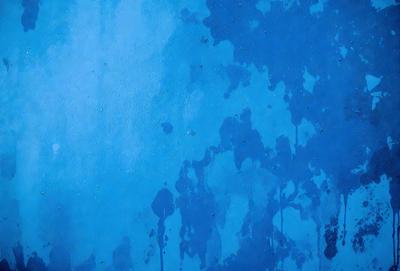 The primary subject of the image is a blue wall with a pattern of drips and splatters on it. The setting is an indoor environment, possibly a room or a bathroom. The visual style appears to be a combination of a photo and a digital art or illustration, as the drips and splatters are created with a blend of colors and textures. The dominant colors are blue and white, with the blue wall providing a cool and calming atmosphere.