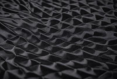 The primary subject of the image is a black fabric with a pattern of waves. The setting is a close-up view of the fabric, showcasing its texture and design. The visual style is a detailed, textured representation of the fabric, which gives it a realistic and intricate appearance. The colors and mood of the image are predominantly black, with the waves pattern adding a touch of contrast and depth to the fabric.