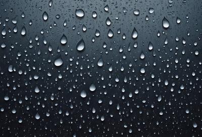 The primary subject of the image is a rainy day, as evidenced by the numerous droplets of water on the black background. The setting is a dark, cloudy sky, which adds to the overall mood of the scene. The visual style of the image is a close-up of the raindrops, showcasing the intricate patterns and details of the water droplets. The colors in the image are predominantly black, with the droplets being the only visible color, creating a moody