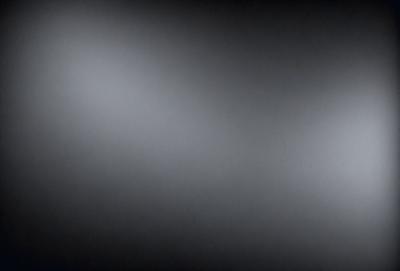 The image is a black and white photo of a dark room. The primary subject is a large, bright light source, which is located in the upper left corner of the image. The setting is a dark room, and the visual style is a black and white photo. The colors and mood of the image are predominantly dark and moody, with the bright light source being the only notable element of color.