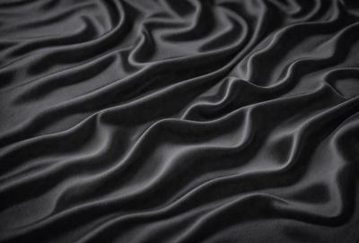 The primary subject of the image is a black fabric with a pattern of waves. The setting is a black background, and the visual style appears to be a photo. The dominant colors are black and grey, creating a moody atmosphere.