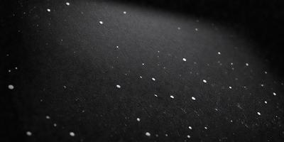 The primary subject of the image is a black surface with white specks on it. The setting appears to be a dark room, and the visual style is a close-up of the black surface. The dominant colors are black and white, creating a contrasting and somewhat mysterious atmosphere.