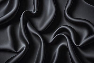 The primary subject of the image is a close-up of a black fabric, possibly a piece of clothing or a curtain. The setting is a dark room, and the visual style appears to be a photo. The dominant colors are black, and the overall atmosphere is mysterious and dramatic.