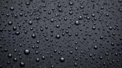 The primary subject of the image is a close-up of a black surface with numerous small bubbles on it. The setting appears to be a dark room, and the visual style is a close-up of the bubbles on the black surface. The colors in the image are predominantly black, and the overall atmosphere is somewhat moody and mysterious.