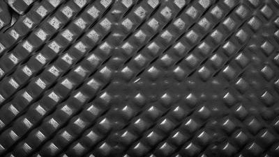 The primary subject of the image is a close-up of a black and silver patterned surface. The setting is a black background, and the visual style appears to be a pattern or texture. The dominant colors are black and silver, creating a sleek and modern atmosphere.