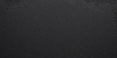 The primary subject of the image is a black surface, which appears to be a beach or a black background. The setting/background is a dark, empty space, which contrasts with the black surface. The visual style of the image is a close-up of the black surface, showcasing its texture and appearance. The colors and mood of the image are predominantly dark, with the black surface being the main focus.